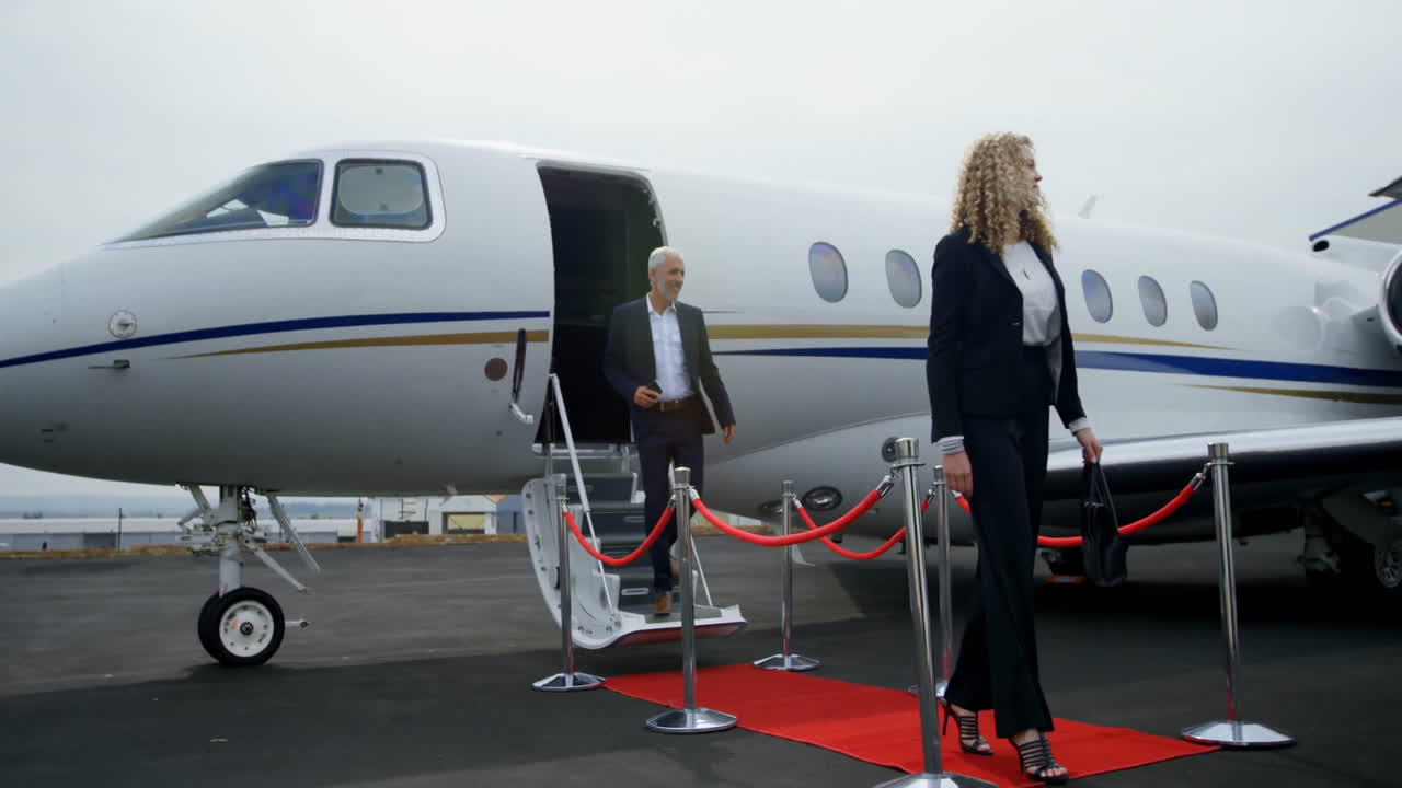 Exiting private jet onto red carpet, man and woman at airport