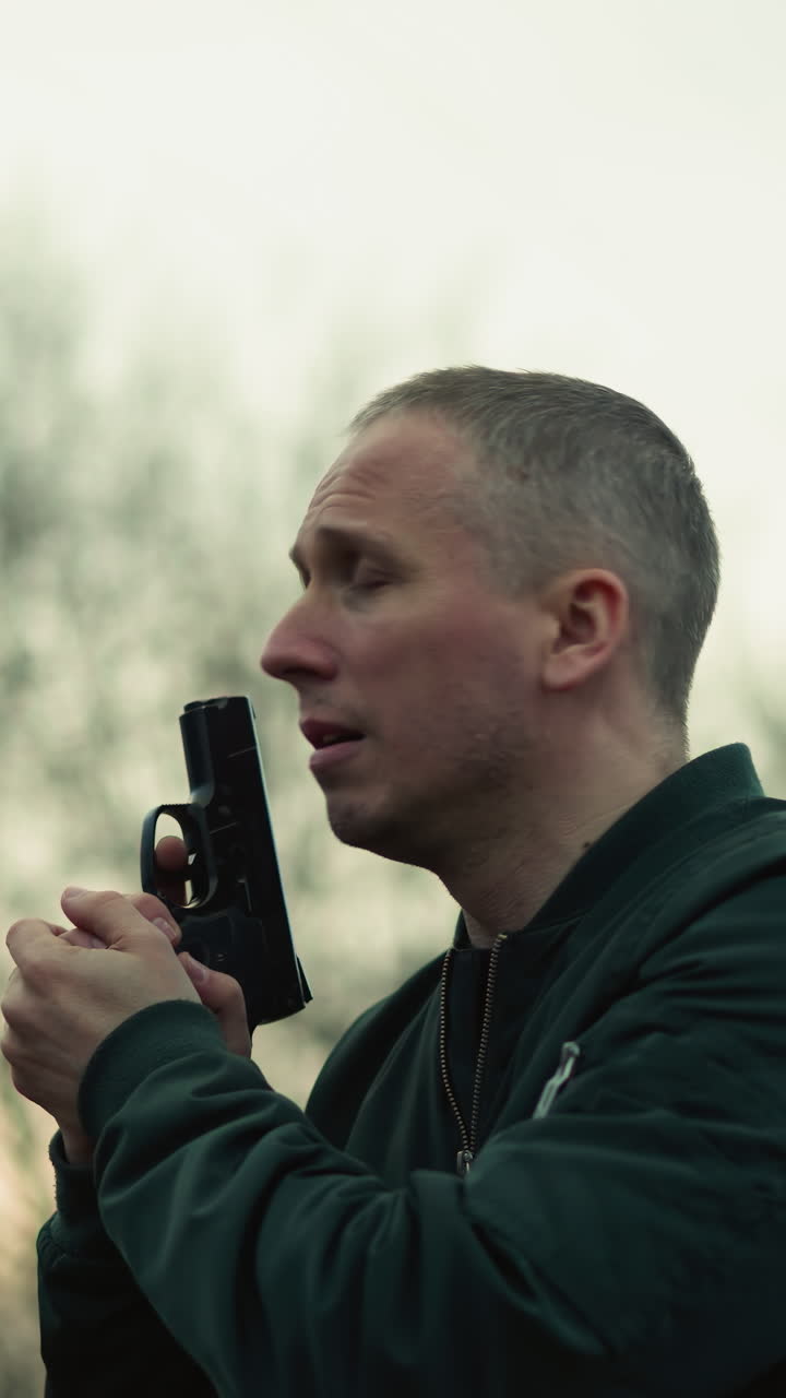 A close view of a man holding a handgun with both hands, looking around, in an outdoor setting with trees in the background