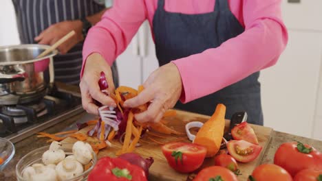 sección media de una pareja mayor diversa que usa delantales y cocina en la cocina