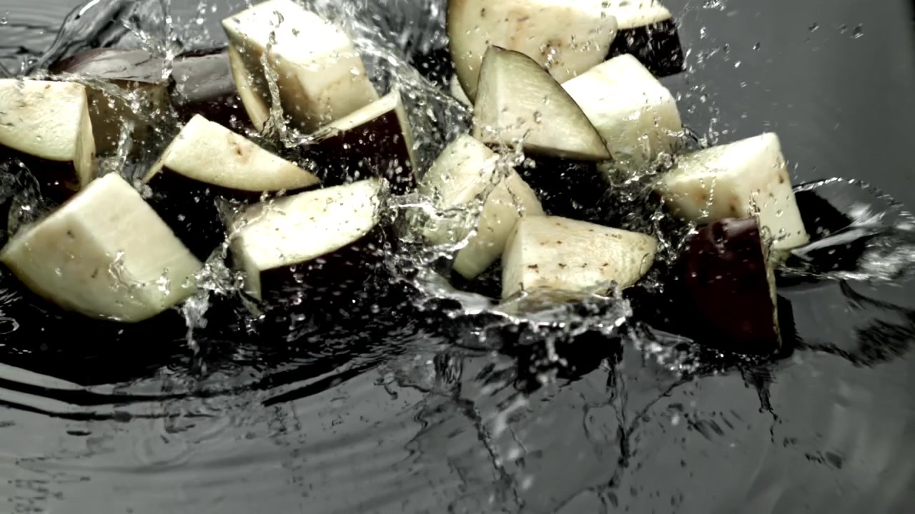 Fersk hakket aubergine som plasker ned i vann i sakte film