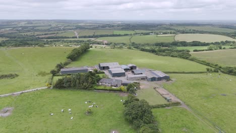 Aerial-view-of-a-rural-farm-small-holding-in-Devon-UK,-surrounded-by-green-fields-and-countryside-scenery