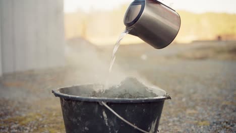 the man is adding hot water to the cement in the bucket for use in the diy hot tub - close up