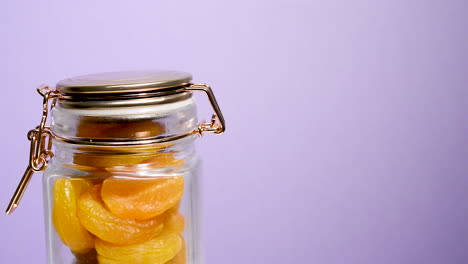 Close-up-of-an-airtight-mason-jar-rotating-with-Turkish-apricot-on-a-neon-lilac-background