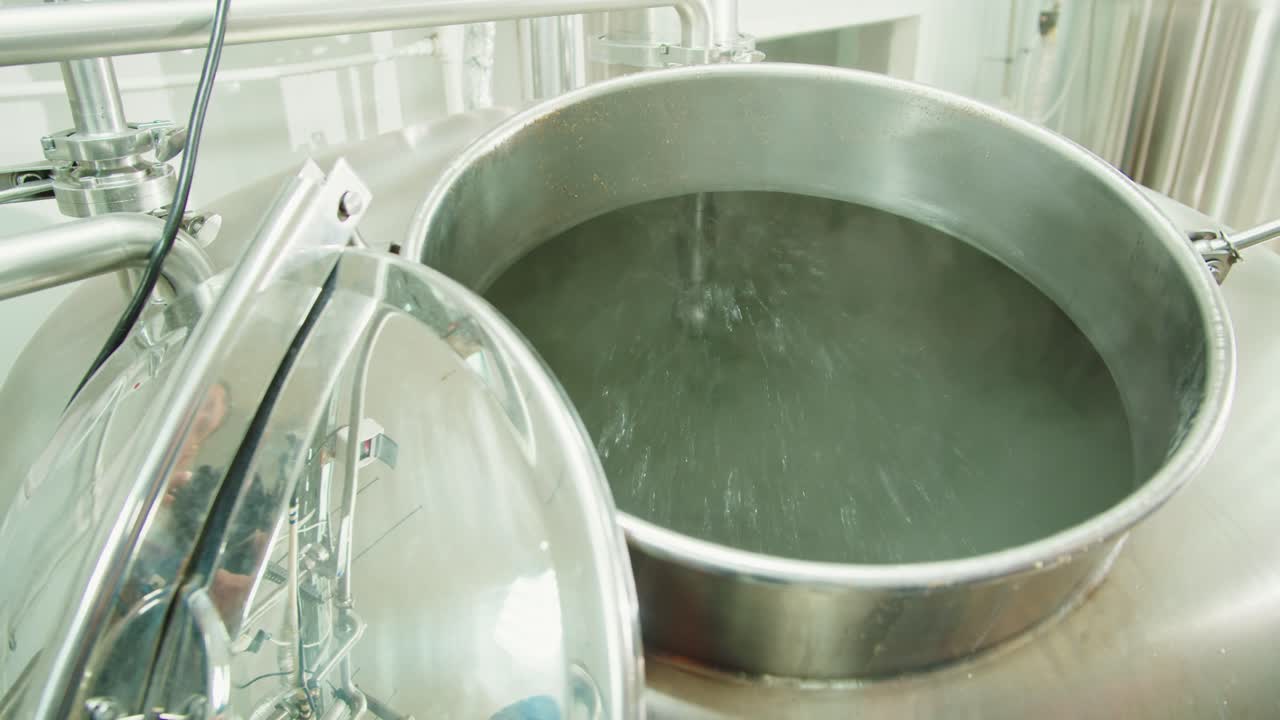 Craft beer production factory, brewery manufacture. Putting barley malt grains in conveyor close-up. Brewing, cooking alcohol in metal vats bottles