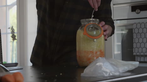 closeup of man inserting freshly vegetables inside jar for fermentation process