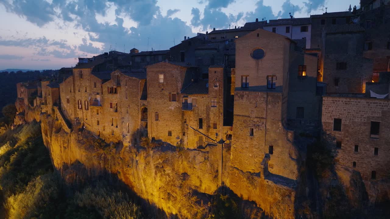 Aerial Drone view of the hilltop Medieval town of Pitigliano, Tuscany at dusk, with the Valdorcia, blinking lights, and twilight sky, in 4K
