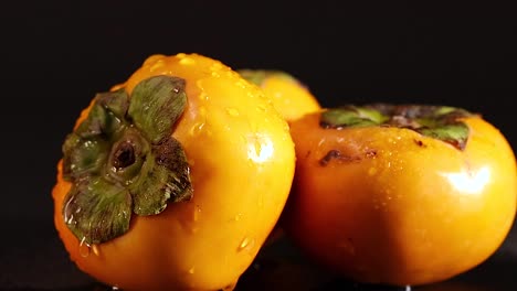 detailed view of water droplets on vibrant persimmons with green calyx, set against a dark backdrop.