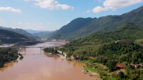 aerial establishing shot of brown coloured mekong river in luang prabang with bridge crossing it