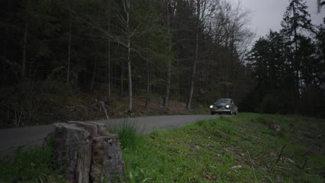A-vintage-car-drives-along-a-forested-asphalt-road