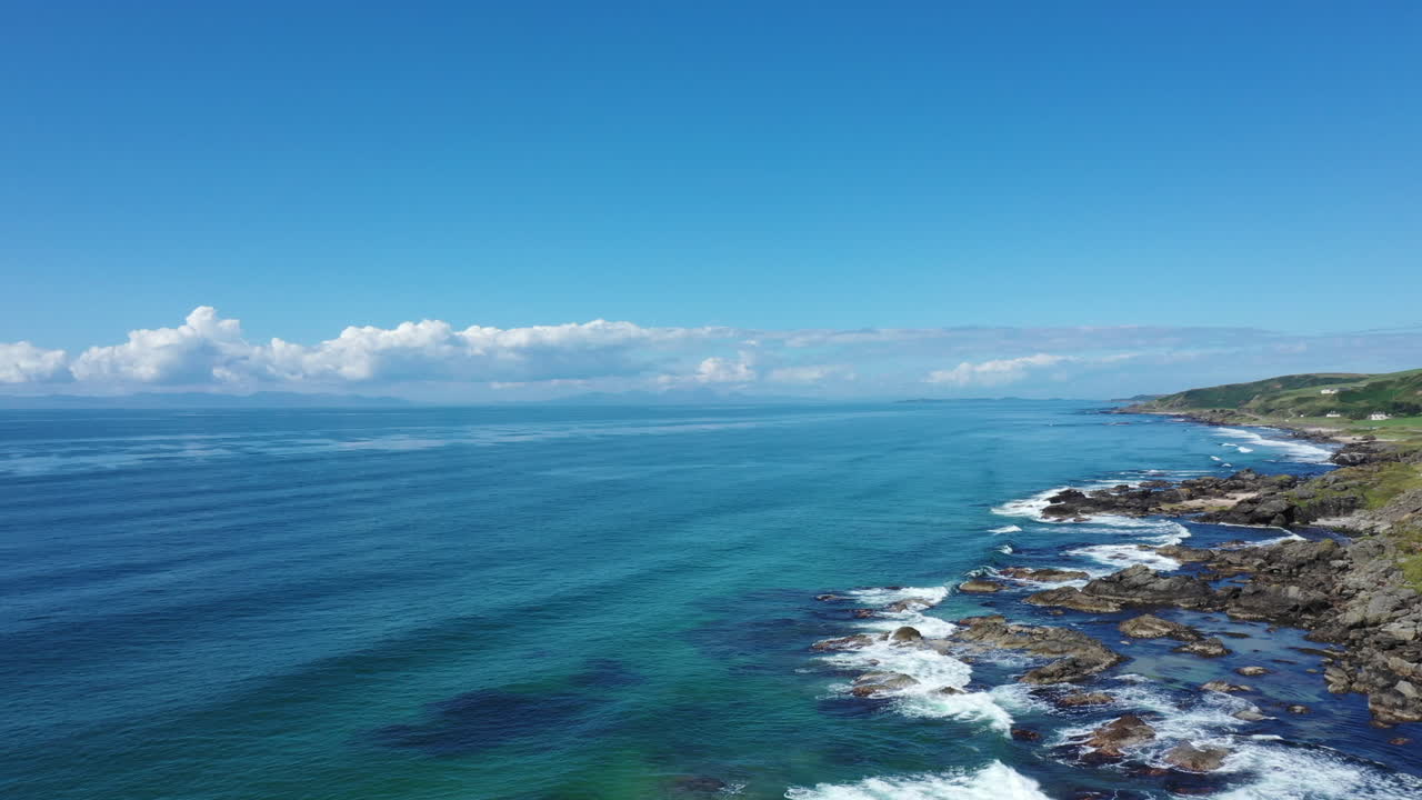 푸른 하늘과 푸르키즈색 바다와 함께 서쪽 스코틀랜드의 바위 해안선을 따라 이동하는 공중 촬영