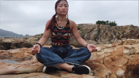 girl meditating cross-legged on a seaside rock outdoors on an overcast day