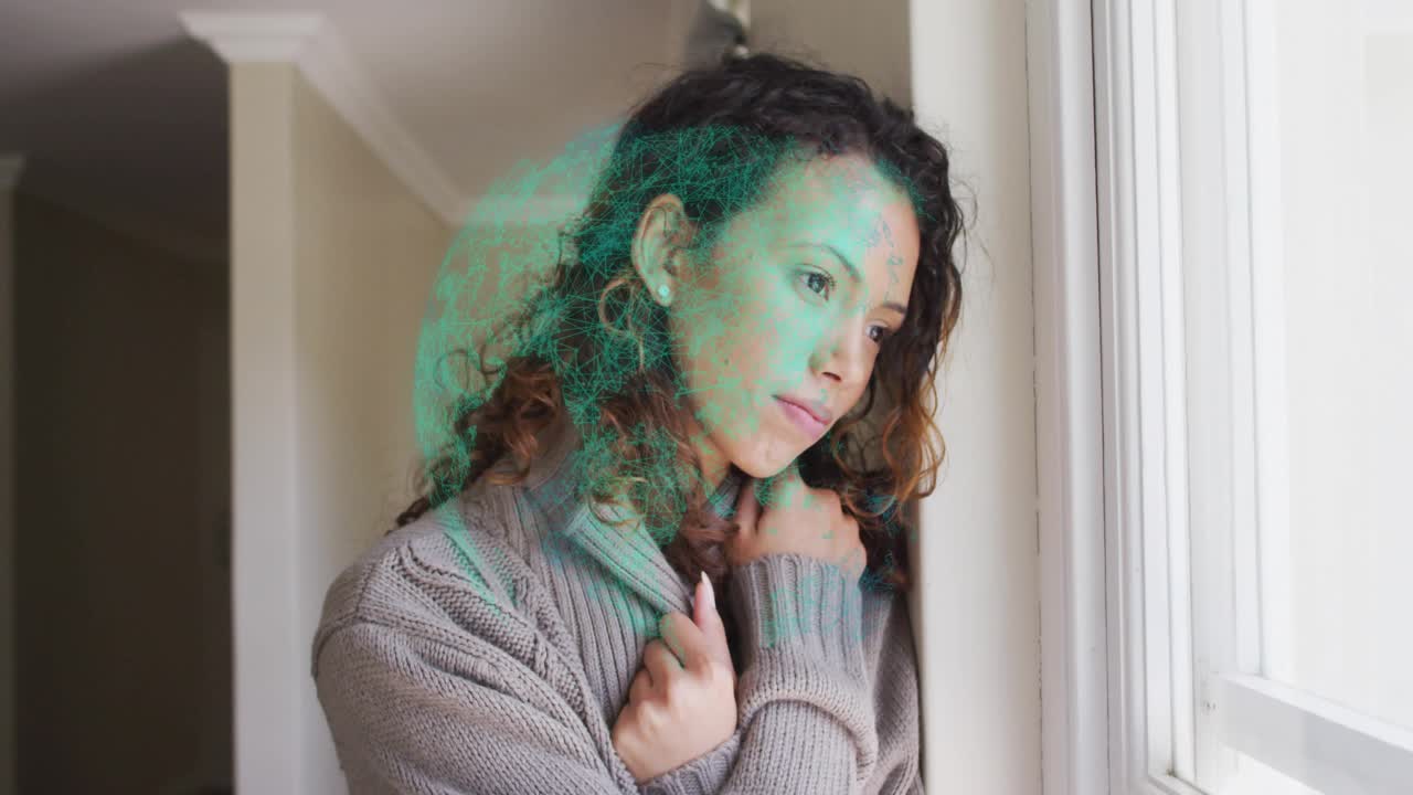 Donna che stringe la felpa con cappuccio alla finestra, tira il cordino stringendo il cappuccio e rivelando una sovrapposizione tecnologica verde