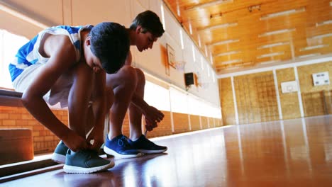 dos escolares atando cordones de zapatos en la cancha de baloncesto