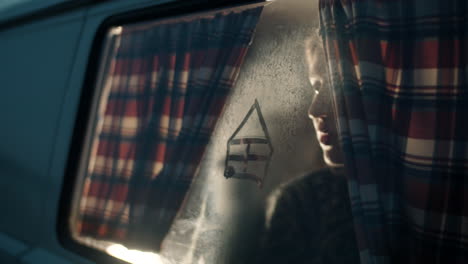 woman drawing house on fogged window glass of camper van