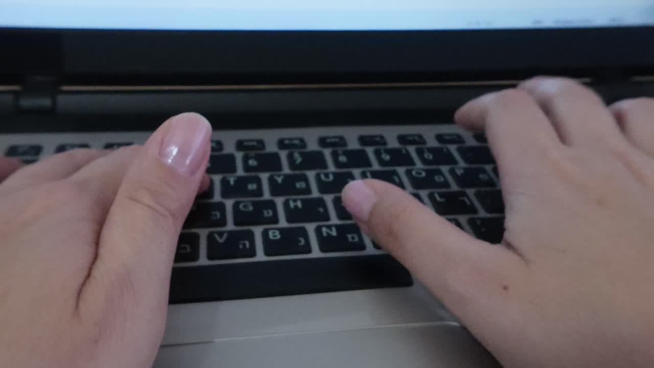 Detailed front view close-up of hands on a laptop keyboard, fingers pressing keys.