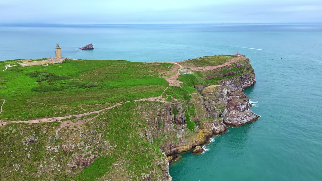 Aerial approach to Cap Fréhel with cliffs, lighthouse, green slopes and coastal trail. Brittany in France. Drone forward