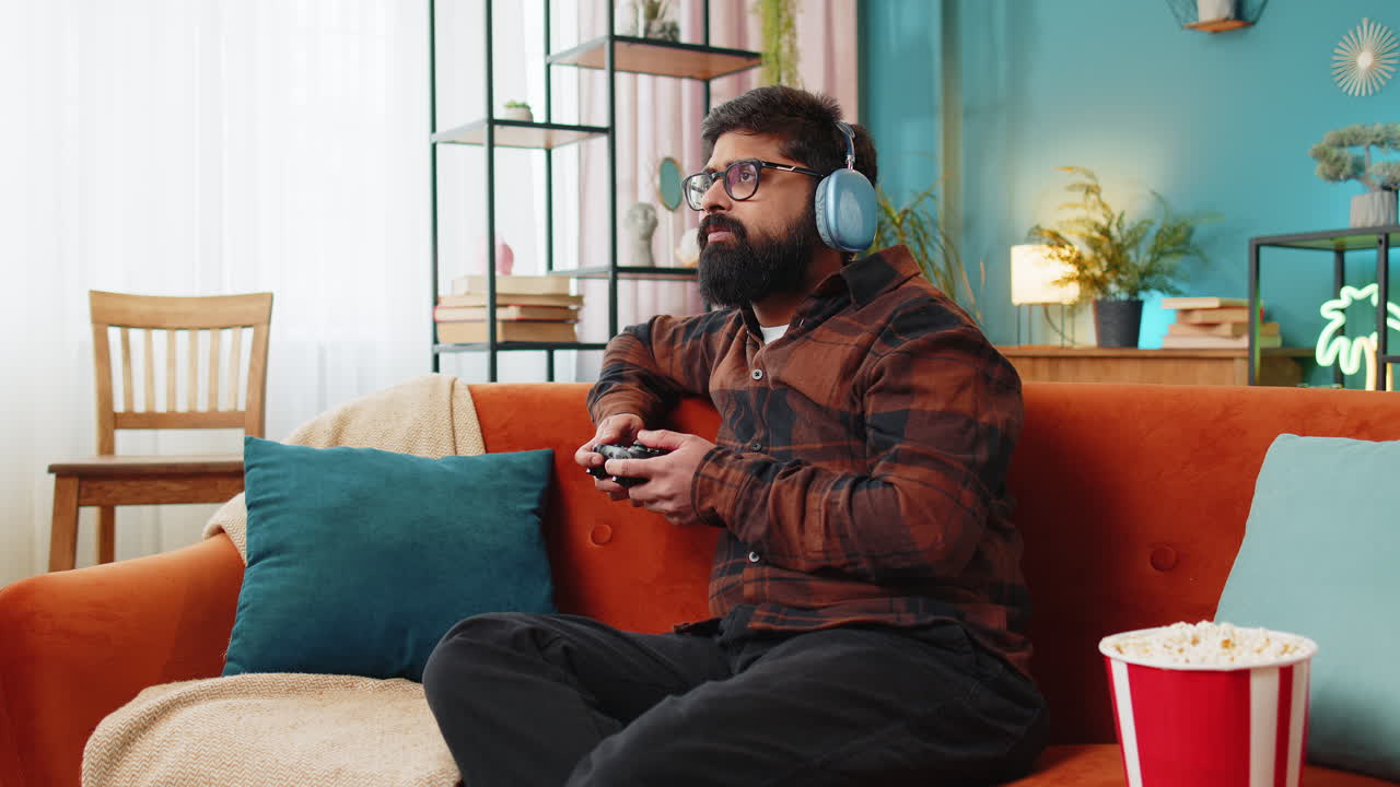 Indian excited man using joystick controller playing video console game online game on home sofa