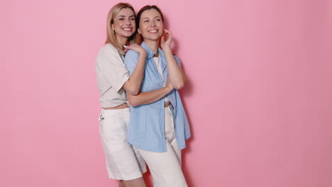 dos mujeres posando contra un fondo rosa