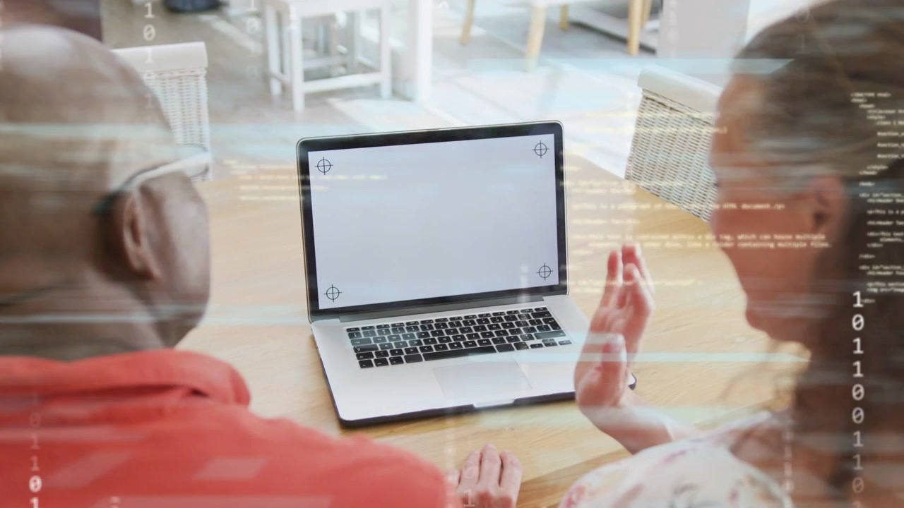 Casal sentado à mesa, mulher gesticulando sobre o laptop, ativando efeito glitch enquanto testa tecnologia.