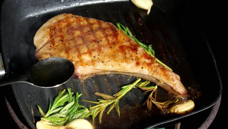 basting steak-pork chop with butter, rosemary and garlic on hot pan, slow motion, close up