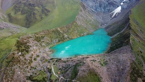 aerial, descending, drone shot panning towards crystal clear, turquoise water of lake humantay, andes mountains, cloudy day, in peru, south america