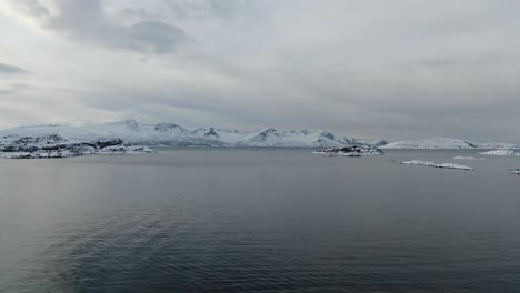 Drohnenansicht-In-Der-Gegend-Von-Tromsø-Im-Winter,-Die-über-Einen-Schneebedeckten-Berggipfel-Und-Ins-Meer-In-Norwegen-Fliegt