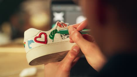 male artist working on colourful design of footwear in loft showroom. fashion designer customising pair of shoes. post production concept. over the shoulder close-up