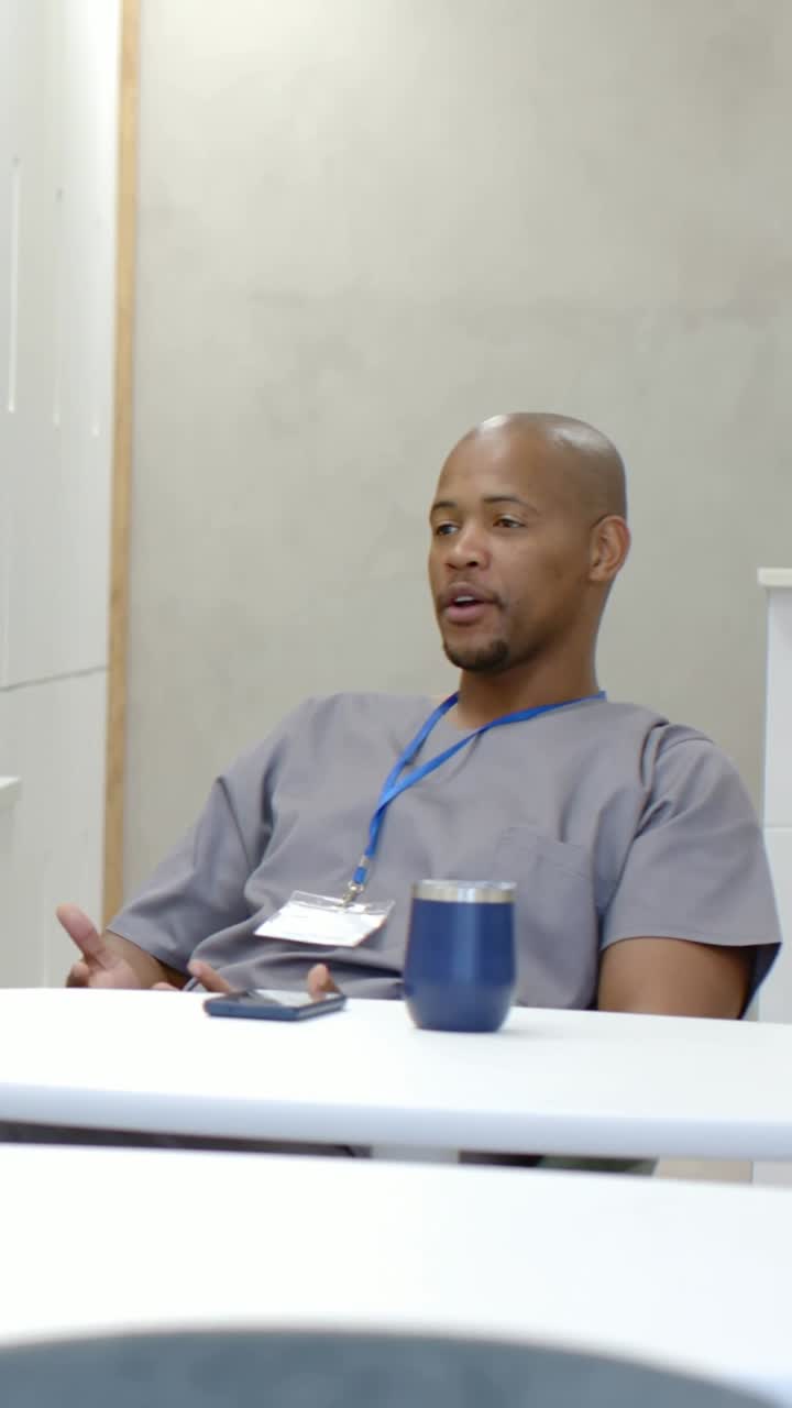 Vertical video: Lip licking man grey scrubs ID badge talking with cell at staff meeting, copy space
