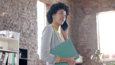 Empresaria-Casual-Birracial-Enfocada-Hablando-Por-Teléfono-Inteligente-Y-Sosteniendo-Archivos-En-Cámara-Lenta