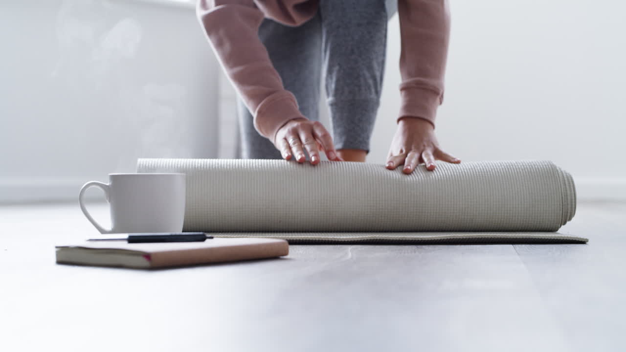 mujer enrollando una alfombra de yoga en casa