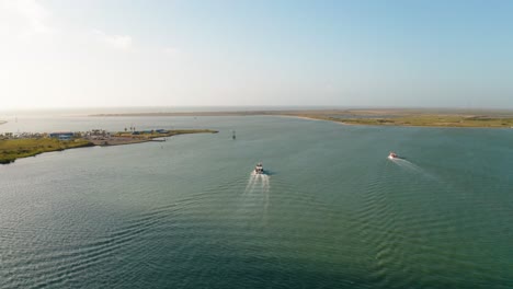 Aerial-drone-flyover-of-boats-leaving-the-bay-harbor-inlet-on-South-Padre-Island,-Texas-coastline