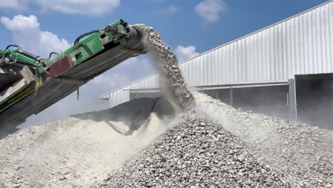 crushed rocks and concrete coming off the belt of a rock crusher creating huge clouds of dust