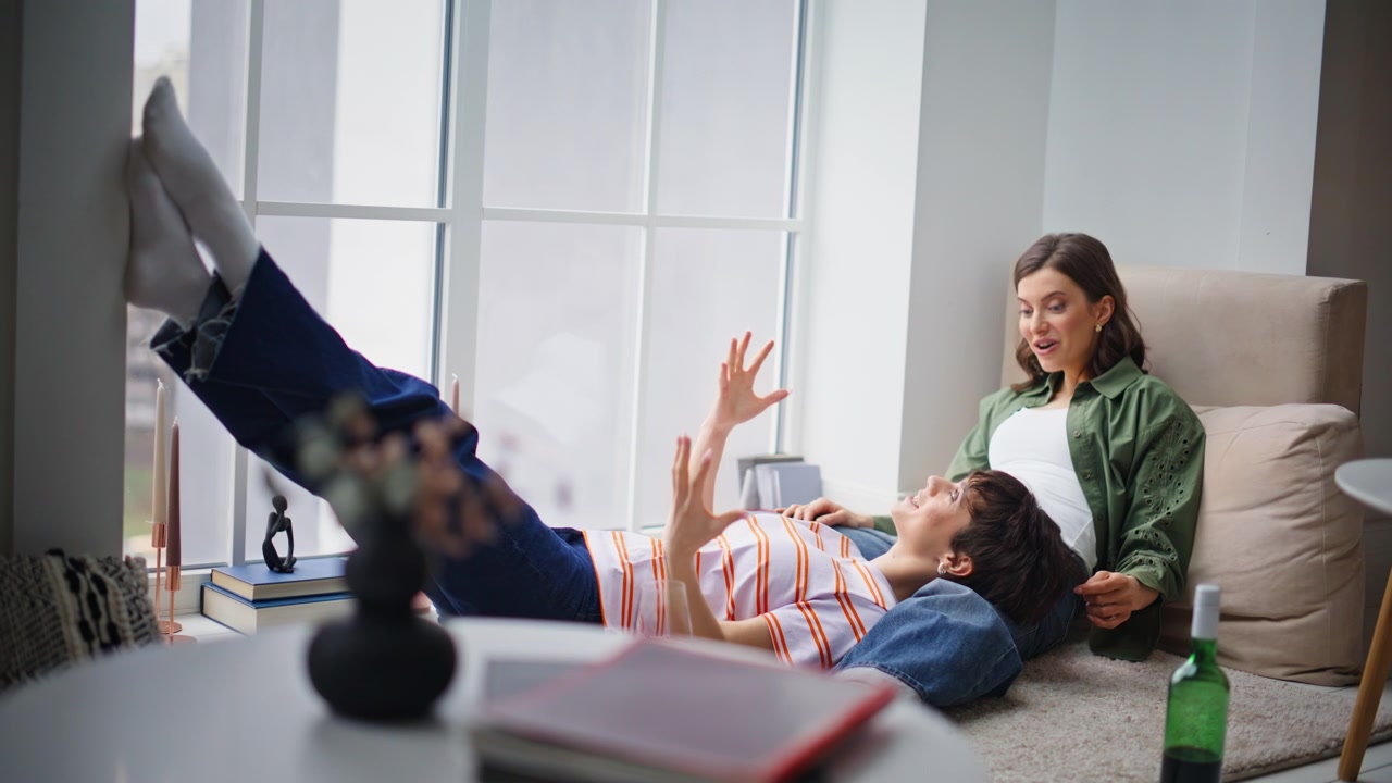 Happy friends sharing conversation in apartment. Happy woman lying partner knee