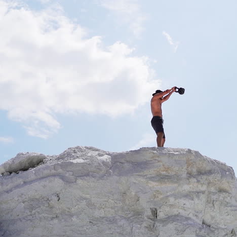 side view of a strong man lifting kettlebell on white hill. male athlete swinging kettlebell with two hands on the beautiful natural background outdoors.
