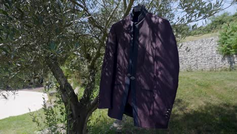 slow orbiting shot of a the grooms wedding suit hanging on a tree in the garden