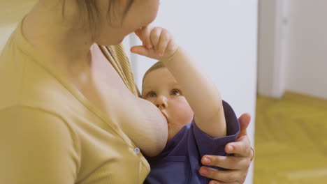 close up of a loving young mother breastfeeding and playing with her baby boy at home