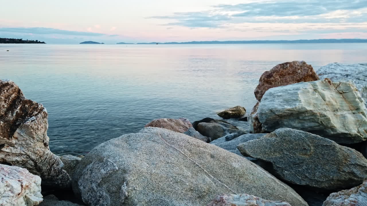 Rocks on the Aegean sea coast at sunset, land in the distance in Greece
