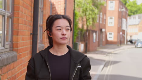 young woman on urban street wearing wireless earbuds exercising warming up for run