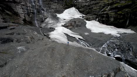 Drohnenansicht-Eines-Mannes,-Der-Auf-Einem-Hügel-Feiert,-Und-Spektakuläre-Aussicht-Auf-Schnee-Und-Wasserfälle