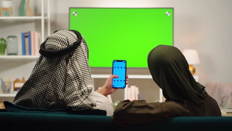 middle eastern couple watching green screen tv and using a smartphone