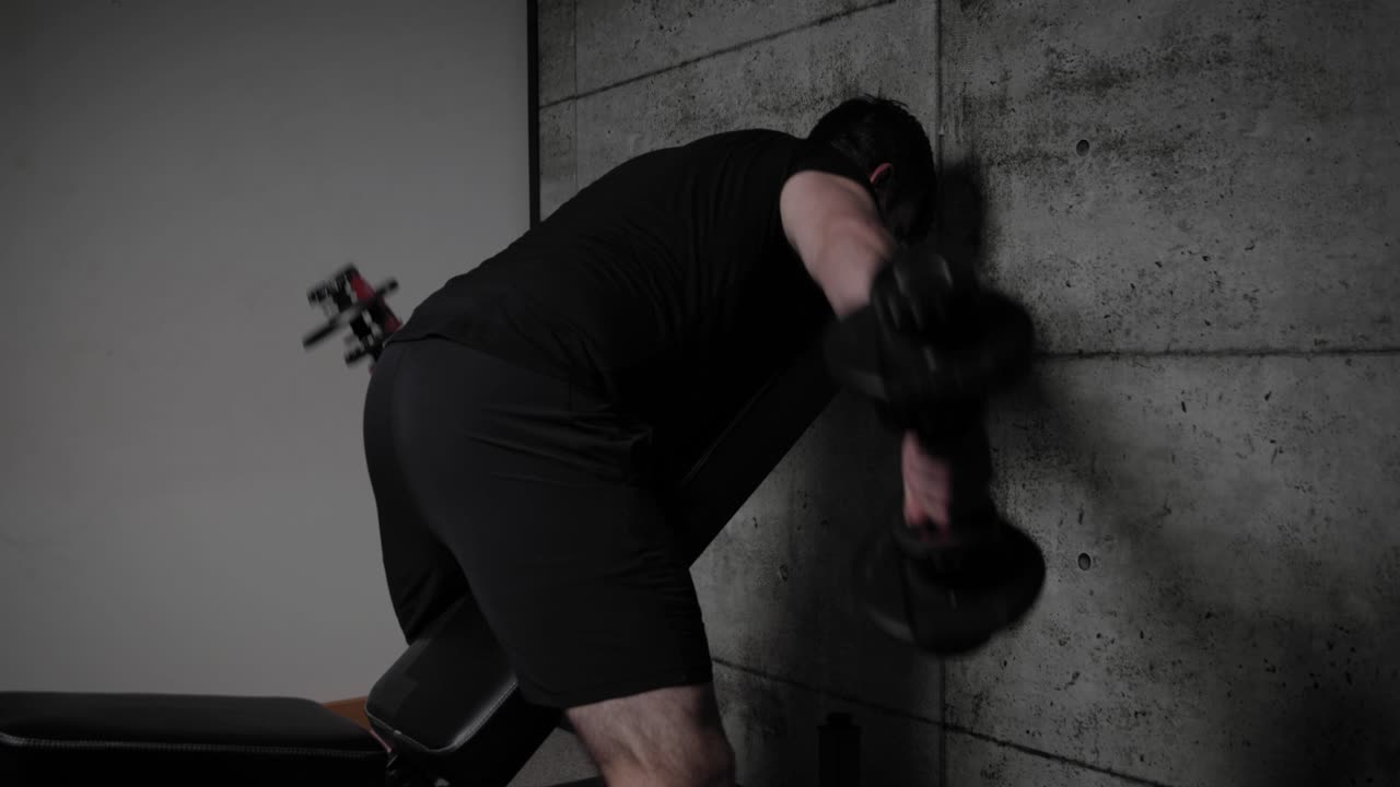 덤벨 측면 델타이드 상승, 영화적 조명, 검은 체육복을 입은 백인 남성