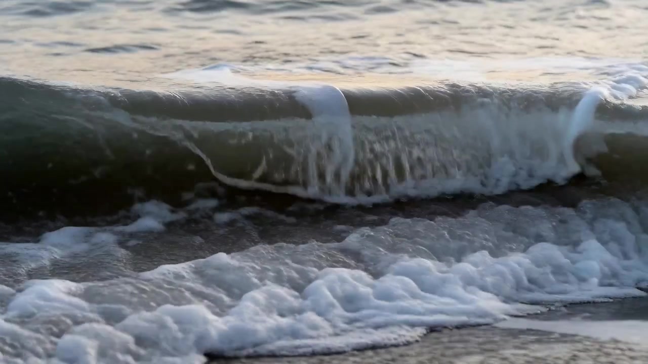 Surging swell pushing dark green wave lip curling and spilling onto wet sandy shoreline, foaming