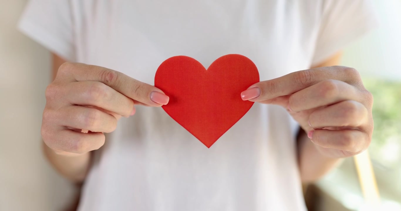 Manos femeninas muestran un corazón de papel rojo, primer plano