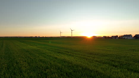 Campos-Verdes-Con-Turbinas-Eólicas-Al-Atardecer,-Casas-A-Lo-Lejos,-Serenas-Y-Amplias