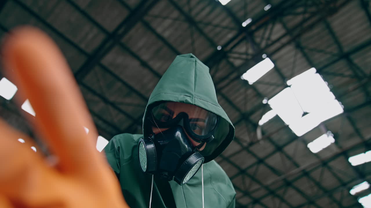 Portrait of a woman in safety suit and gas mask. Human wearing antibacterial costume trying to touch something with hand in glove in abandoned place. Gas attack.
