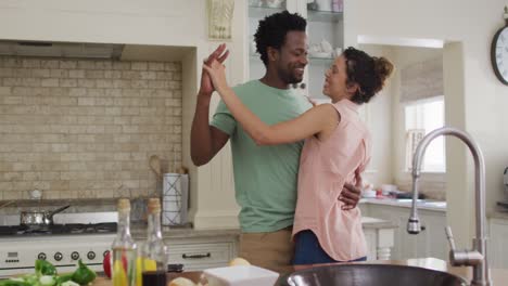 feliz pareja biracial bailando juntos en la cocina