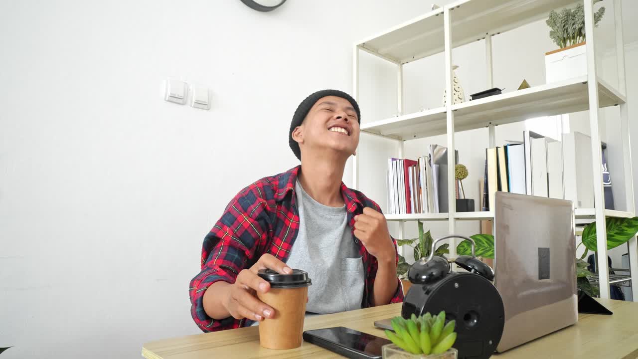 Young Asian Male Entrepreneur Sitting At Desk Looking At Laptop Screen, Raising Hands With Excitement Celebrating Success Selling
