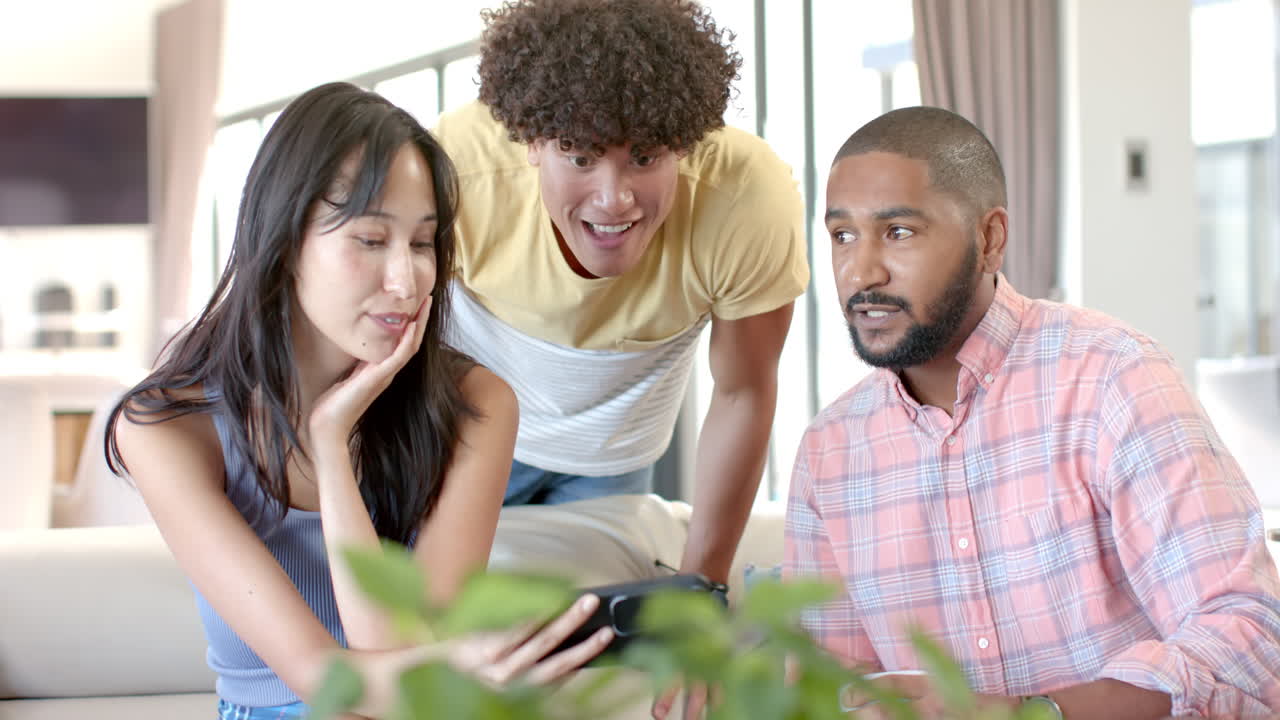 At home, diverse friends hanging out, looking at smartphone and discussing something together