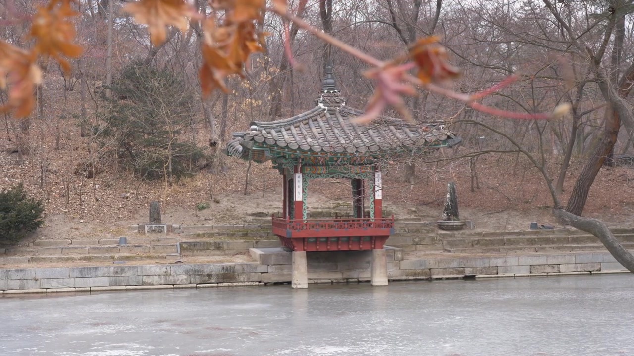Ripresa paesaggistica al rallentatore di un antico padiglione del tempio adagiato su un lago ghiacciato con boschi sullo sfondo. Cortile del Giardino Segreto al Palazzo Changdeokgung, città di Seoul, Corea del Sud. Viaggi, natura.