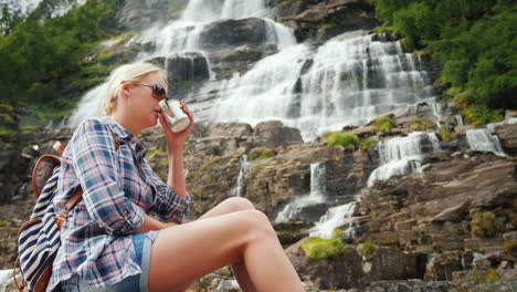 young woman drinks water on the background of the twin waterfall tvindefossen in norway clean drinki